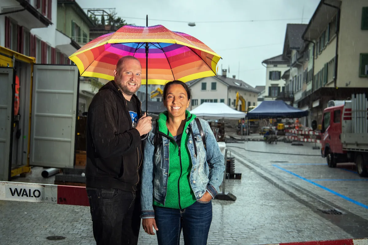 Hier ist Claudia Knecht mit Dominik Gross zu sehen. Gemeinsam riefen sie den Pfäffiker Wochenmarkt ins Leben. Ein Mann und eine Frau stehen unter einem Regenbogenschirm.